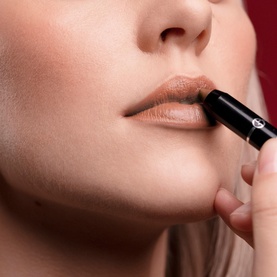 Model with Armani Beauty Color Sketcher lipstick in Amaretto being applied to lips, warm nude-brown shade shown on fair skin tone