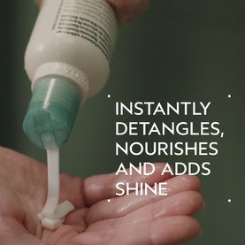 AVEDA Shampure&trade; Nurturing Conditioner 50ml being dispensed from pump bottle onto open palm, white cream texture visible