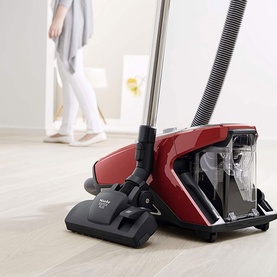 Miele Blizzard CX1 Cat & Dog Vacuum Cleaner in red, bagless canister design with floor brush head, shown in use on light wood flooring