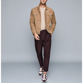 Model wearing Reiss Bless Regular Fit T-Shirt in beige, styled with a tan suede jacket, dark burgundy trousers, and multicolour trainers
