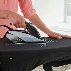 Braun TexStyle 5 Steam Iron in use on dark fabric, releasing steam on an ironing board, held by a person in a pink top