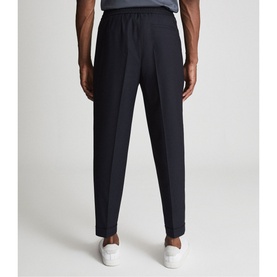 Model wearing Reiss Brighton Pleat Front Trousers in blue, shown from behind, with white trainers visible at hem