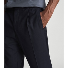 Model wearing Reiss Brighton Pleat Front Trousers in navy blue, cropped view showing pleat detail and side pockets, styled with grey top
