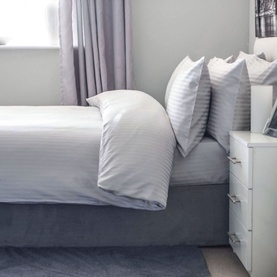 Belledorm Hotel Suite 540 Flat Sheet in Platinum metallic, styled on a made bed with matching pillowcases in a neutral bedroom setting