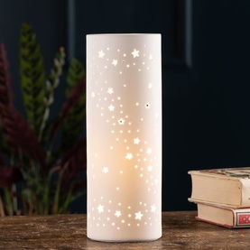 Belleek Starry Night Luminaire in cream porcelain, cylindrical table lamp with cut-out star pattern, glowing warmly on wooden surface