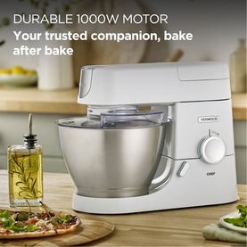 Kenwood Chef stand mixer in white with silver mixing bowl, shown on kitchen counter alongside pizza and olive oil