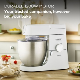 Kenwood Chef XL 6.7L 1200W Food Mixer in white with stainless steel bowl, shown on kitchen worktop with baking ingredients nearby.