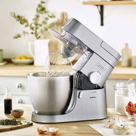 Kenwood Chef XL 6.7L 1200W Food Mixer in silver, shown mid-mix with whisk attachment, styled on a kitchen countertop with baking ingredients
