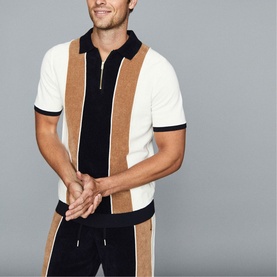 Model wearing Reiss Claude Stripe Zip Neck Polo Shirt in blue with camel and white vertical stripes, styled with matching trousers