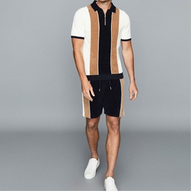 Model wearing Reiss Claude Stripe Zip Neck Polo Shirt in blue, styled with matching navy shorts and white trainers
