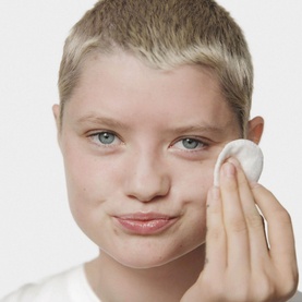 Model applying Clinique Clarifying Lotion with a cotton pad to cheek, exfoliating toner for oily skin