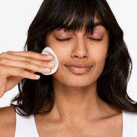 Model with Clinique Clarifying Lotion applied via cotton pad to cheek, eyes closed, white top visible