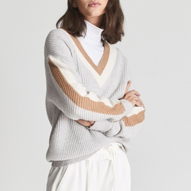 Model wearing Reiss Cora Colour Block Cricket Sweater in grey with camel and white stripe detail, styled with white trousers and roll neck