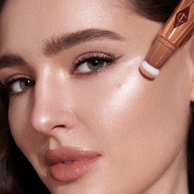 Model with Charlotte Tilbury Hollywood Beauty Light Wand highlighter applied to cheekbone, shown close up on glowing skin