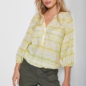 Model wearing Mint Velvet Callie Floral Print Blouse in yellow, styled with khaki trousers. V-neck, button detail, elasticated cuffs
