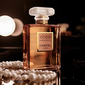 Chanel Coco Mademoiselle Eau de Parfum Spray in amber glass bottle with gold label, styled with pearl necklace on dark background