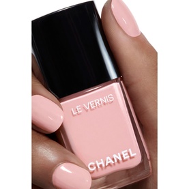 Chanel Le Vernis nail varnish in soft pink, held by hand with matching manicured nails, black square cap