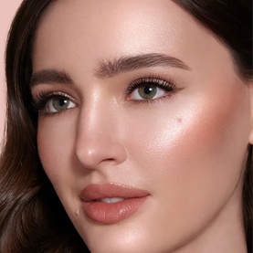 Model with Charlotte Tilbury Beauty Lightwand in Beauty All, showcasing a radiant glowing complexion with soft peachy-pink blush and bronzed skin.