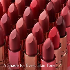 Charlotte Tilbury KISSING Lipstick in Yes Honey among multiple rosy-red shades in gold cases, with "A Shade for Every Skin Tone" text