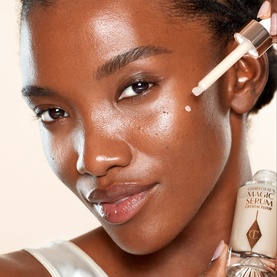 Model with Charlotte Tilbury Magic Serum Crystal Elixir, applying a drop to cheek, showcasing glowing, radiant skin.