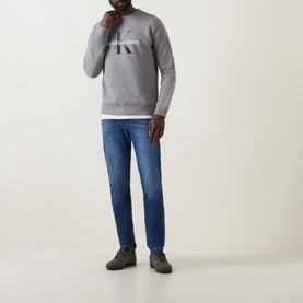 Model wearing Calvin Klein Jeans Monogram Logo Sweat Top in grey, styled with blue jeans and grey trainers