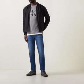 Model wearing Calvin Klein Jeans Monogram Logo Sweat Top in grey, styled with black zip-up jacket and blue slim-fit jeans