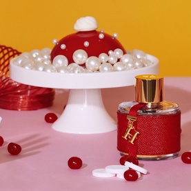 Carolina Herrera CH Woman Eau de Toilette in red leather-wrapped bottle with gold hardware, styled with pearls and red berries on pink surface