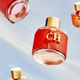Carolina Herrera CH Woman Eau de Toilette in red leather-wrapped bottle with gold CH logo, surrounded by multiple floating bottles against blue sky