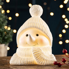 Belleek Cosy Snowman LED Light in white ceramic, glowing warm light, wearing knitted hat and scarf, set on wooden surface with bokeh lights