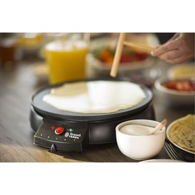 Russell Hobbs Fiesta Crepe Maker in use on kitchen counter with batter being spread, alongside bowl of cream and orange juice