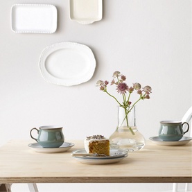 Denby Regency Green Tea/Coffee Cup and saucer styled on wooden table with cake, flowers, and white platters on wall behind