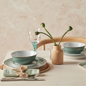 Denby Regency Green tableware set styled on a dining table with woven placemat, clear glass, and dried poppy stems in a wooden vase