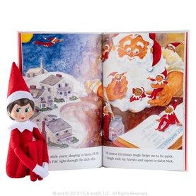 Elf on the Shelf Girl Scout Elf soft doll in red outfit with dark hair, posed beside an open illustrated Christmas storybook