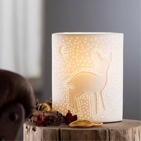 Belleek Fawn Luminaire in white porcelain with cut-out deer and star design, glowing warmly on a wooden surface with festive styling
