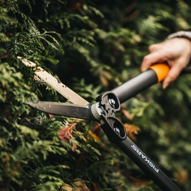 Fiskars PowerGear Hedge Shear HS72 in use trimming a green conifer hedge, with black and orange handles visible