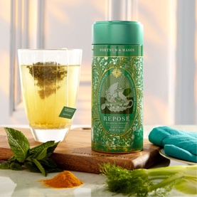 Fortnum & Mason Botanical Infusion Repose Tea Bags in green tin, shown with brewed cup, fresh mint, turmeric and fennel on wooden board
