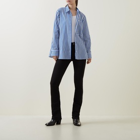Model wearing FRAME DENIM Le Mini Boot High-Rise Jeans in black bootcut fit, styled with a blue striped oversized shirt and black heeled boots