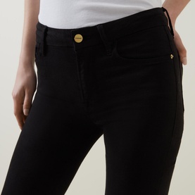 Model wearing FRAME DENIM Le Mini Boot High-Rise Jeans in black, featuring gold-tone button and slim bootcut fit, styled with a white top