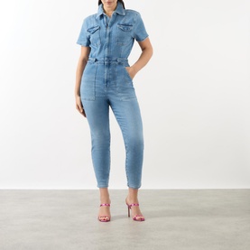 Model wearing Good American Fit For Success Denim Jumpsuit in blue, with pointed collar, capped sleeves and utility pockets
