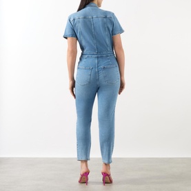 Model wearing Good American Fit For Success Denim Jumpsuit in blue, rear view, with pink heeled mules. Straight leg, capped sleeves