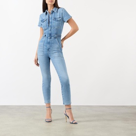 Model wearing Good American Fit For Success Denim Jumpsuit in blue with pointed collar, capped sleeves and utility pockets, styled with silver heels