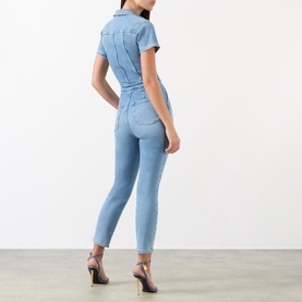 Model wearing Good American Fit For Success Denim Jumpsuit in blue, rear view, styled with strappy black heels