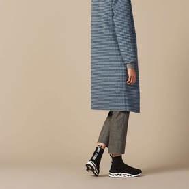 Model wearing Sandro Flame Sock Trainers in black, knit pull-on style with chunky white sole, styled with grey trousers and blue checked coat