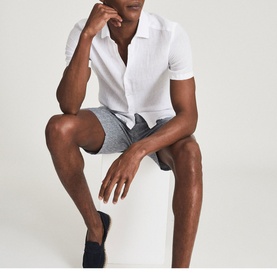 Model wearing Reiss Holiday Linen Slim Fit Shirt in white, short-sleeved, styled with grey shorts and navy loafers