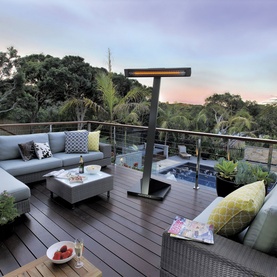 Heatstrip Intense Electric Heater with Stand in black, positioned on a timber deck with outdoor sofa seating and pool at dusk