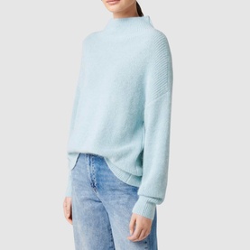 Model wearing Forever New Hester Rib Knit Sweater in blue with stand neck and deep cuffs, styled with light wash jeans