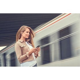 Woman at train platform using smartphone, wearing Jabra Elite 85t True Wireless Earbuds in Black, with blurred train passing behind her