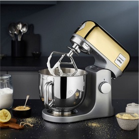 Kenwood kMix Limited Edition Stand Mixer in gold and silver with stainless steel bowl, styled with milk and ingredients on dark countertop
