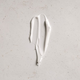 Le Labo Hinoki Hand Lotion texture swatch showing creamy white formula smeared on a light stone surface