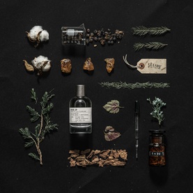Le Labo BAIE 19 Eau de Parfum bottle styled with botanical ingredients including cotton, juniper, pepper, and bark on black background